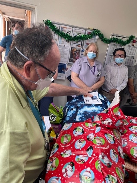 A man wearing a mask opens a gift wrapped in Christmas themed paper.