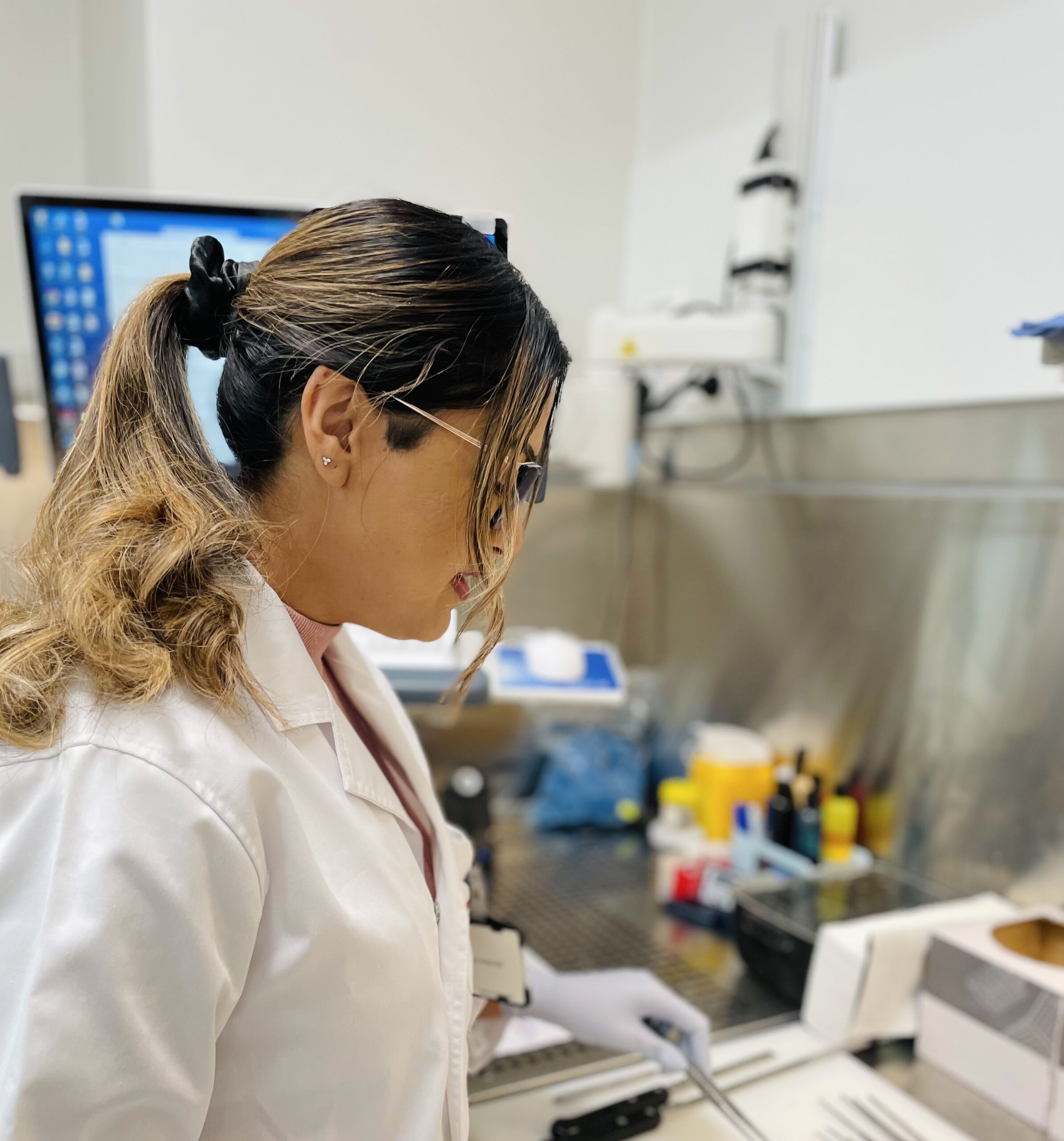 A woman works at a laboratory bench wearing a white lab coat.