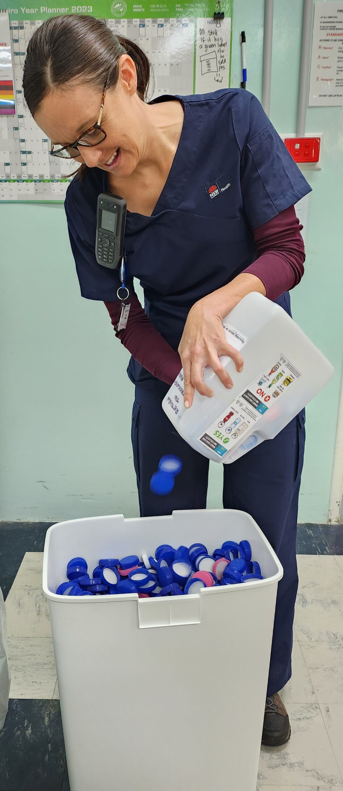 A woman putting plastic bottle lids into a large recycling container.