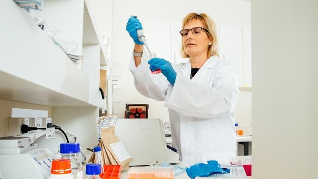 A woman in a white lab coat holding a pipette working in a laboratory.