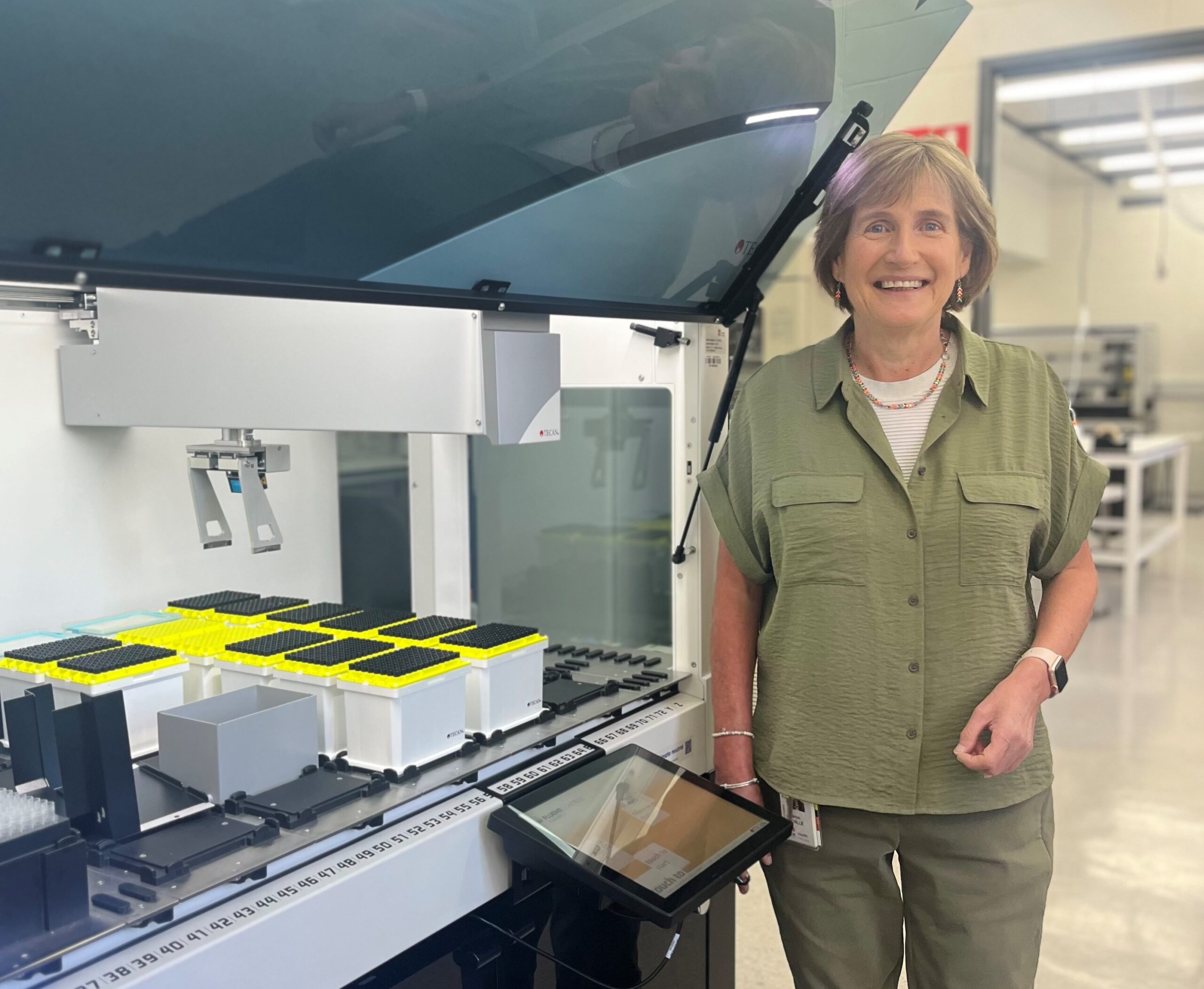 A woman smiling, standing next to a high-tech DNA robotics machine. 