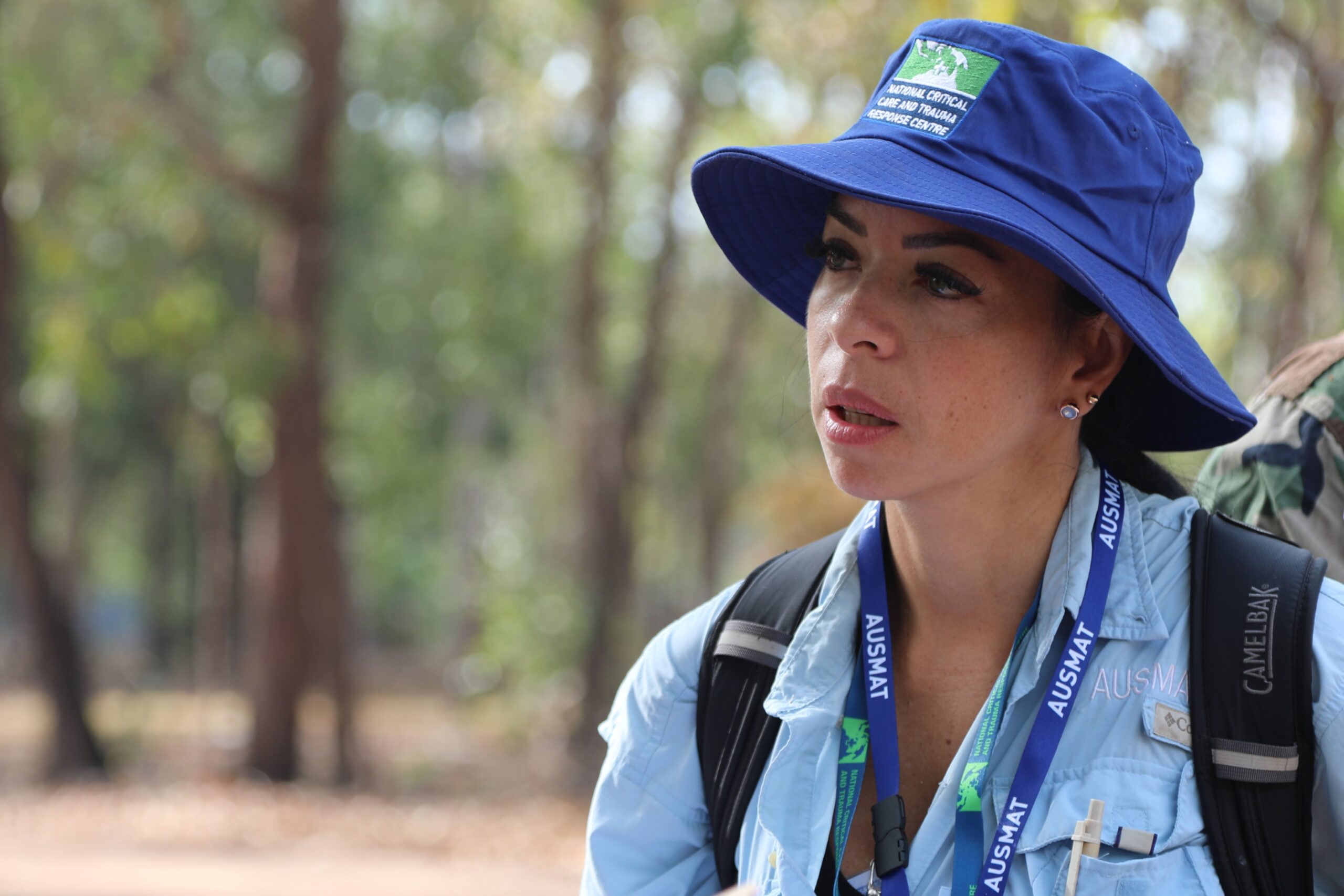 A woman in a uniform and hat in a forested area.