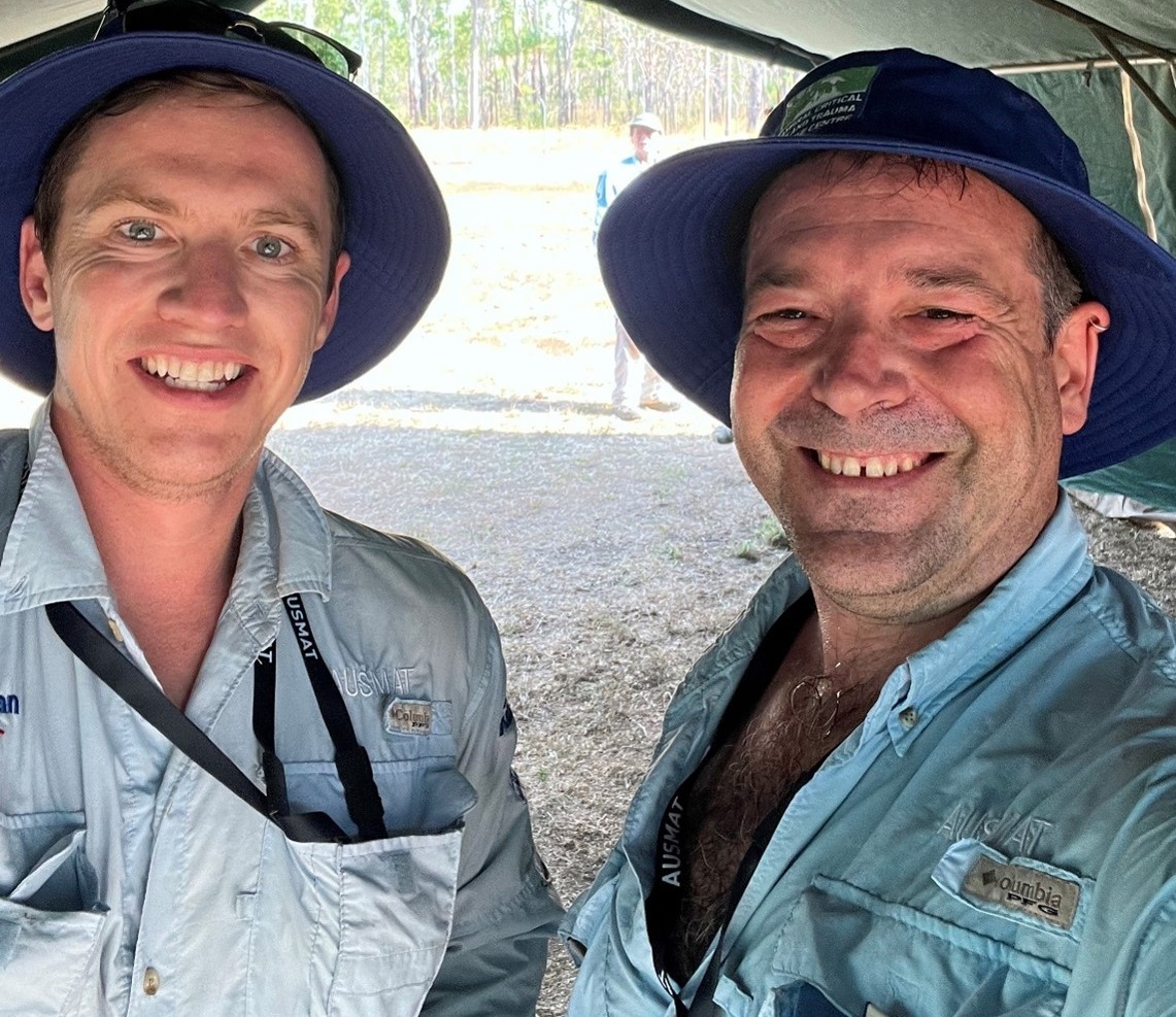 Two men in blue shirts with AUSMAT logos, looking tired and dirty.