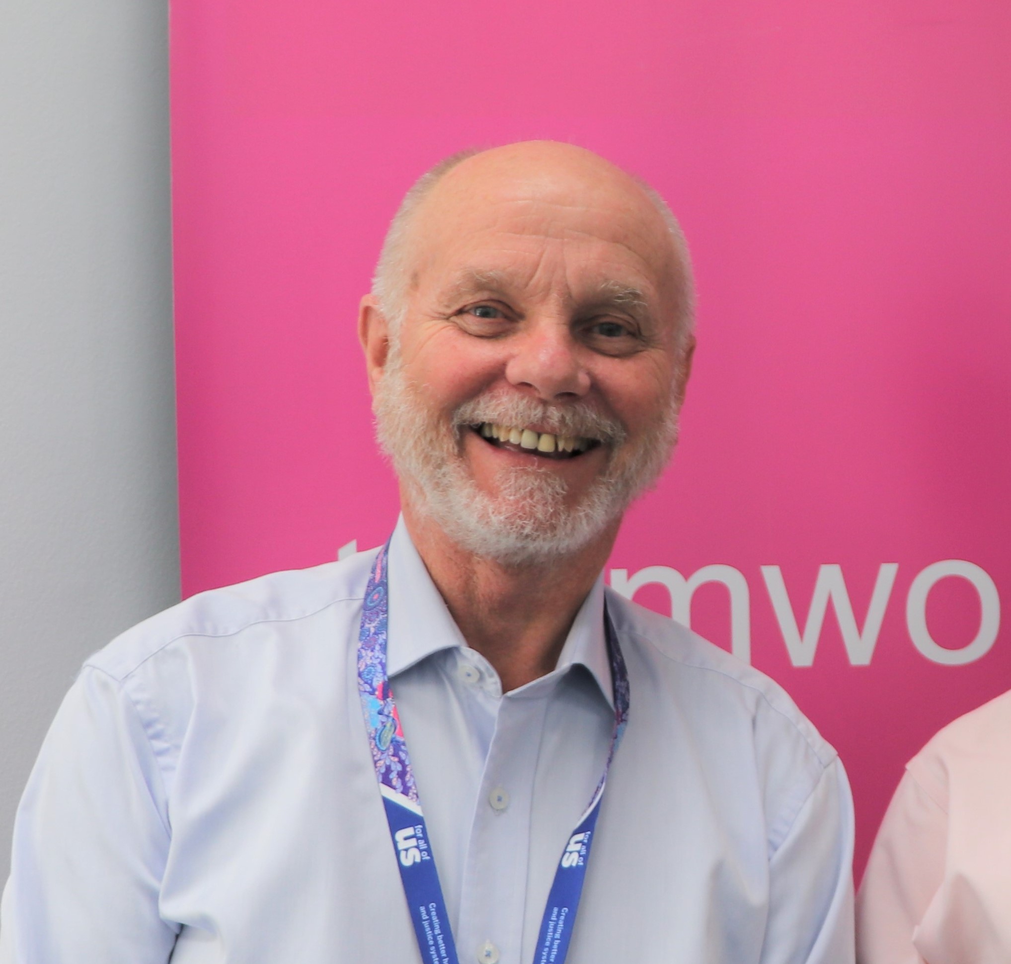 A man smiling in front of  a pink background.