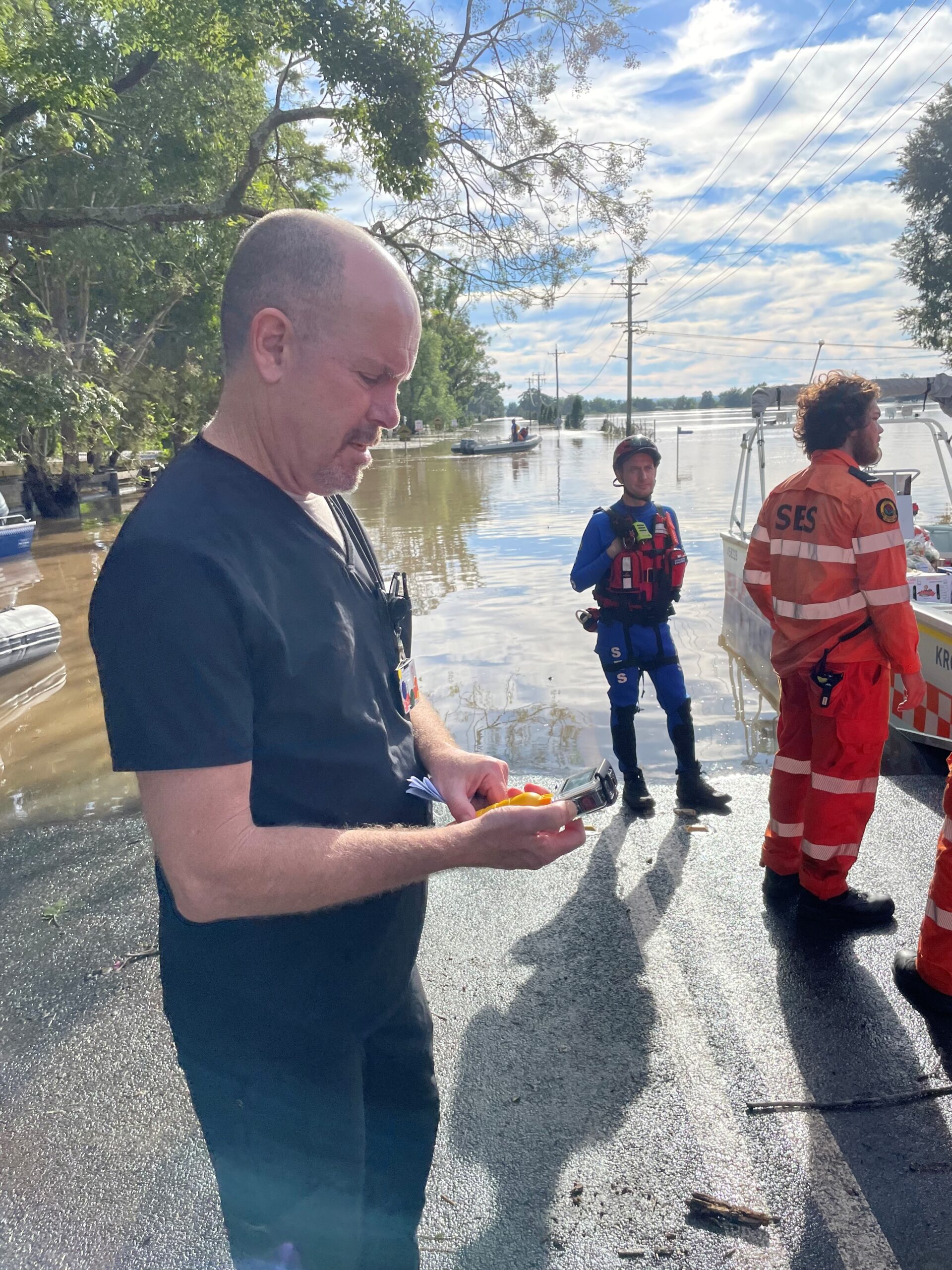 A man standing near floodwaters and SES volunteers.