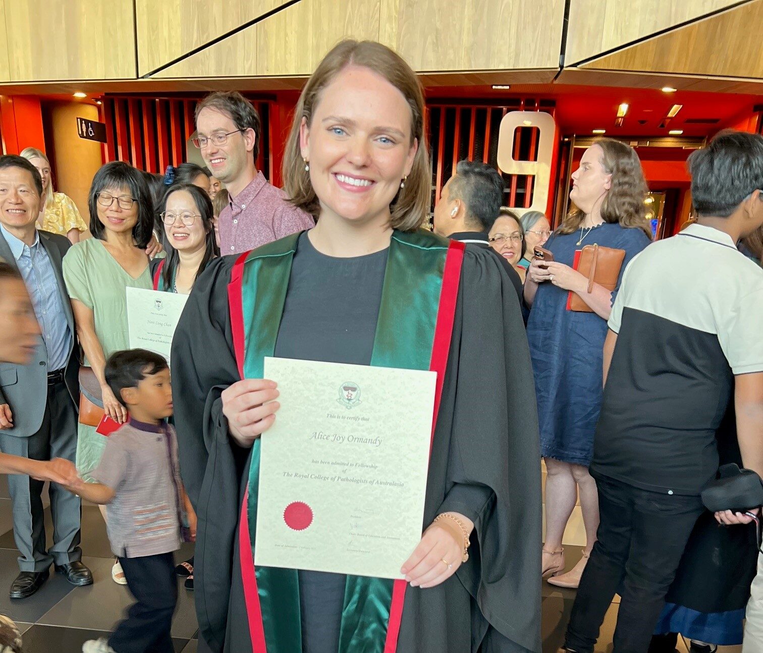 A woman wearing graduation robes holding a graduation certificate.