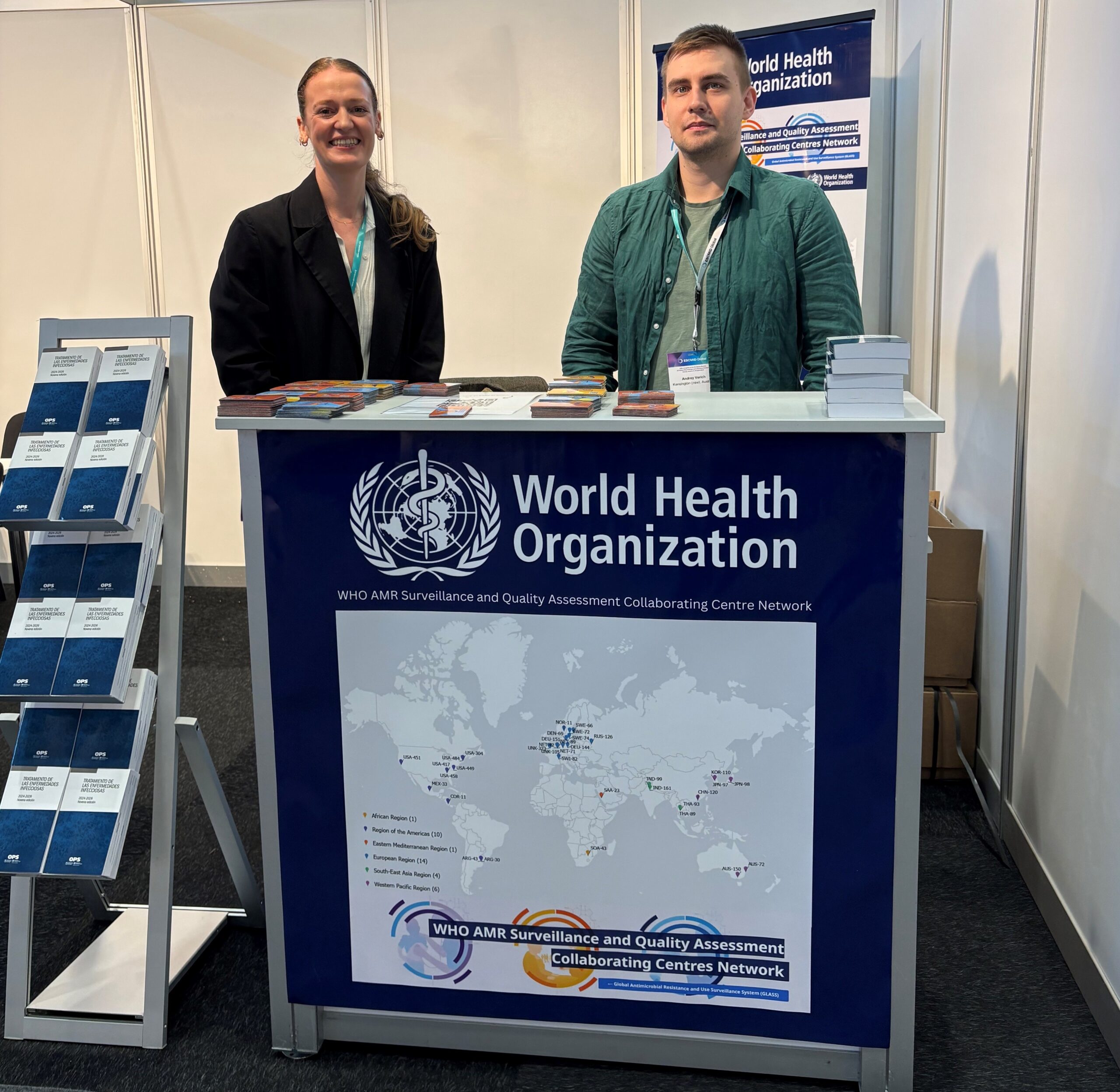 A man and a woman standing at a World Health Organization booth at a conference