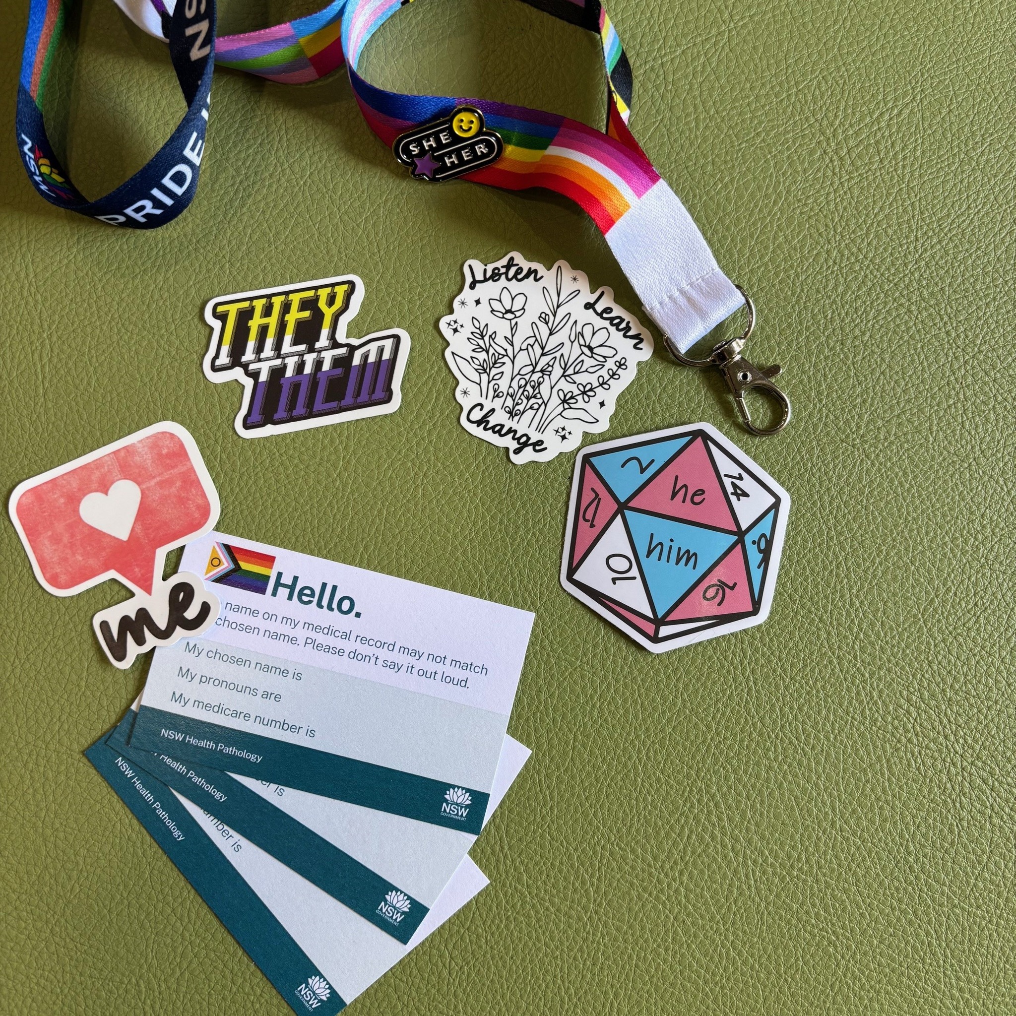 Proud to be Australia’s only silver service health provider for LGBTQIA+ inclusion 1 Business cards and colourful LGBTQIA+ stickers and rainbow lanyards spread out on a green desk.
