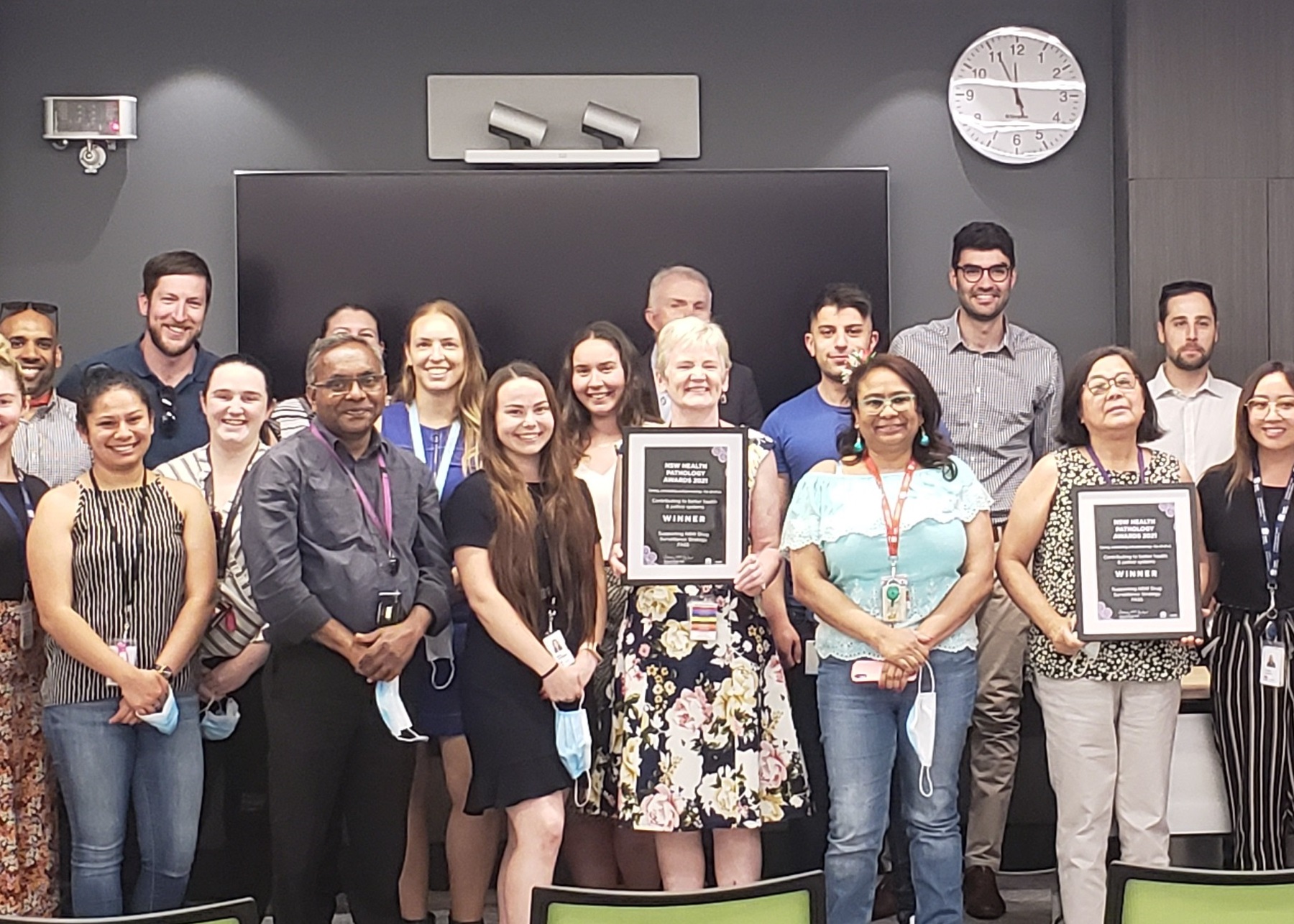 A group of people smiling, with two holding framed award certificates.