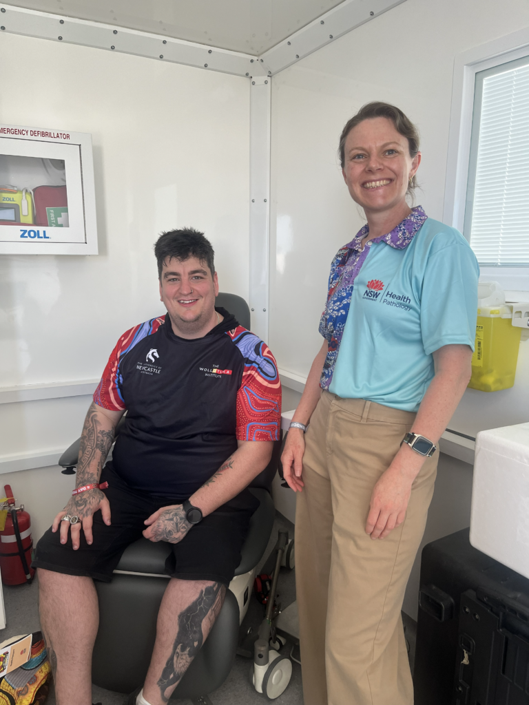 A woman standing next to a man sitting in a chair inside a medical testing van. 